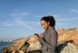 woman in gray long sleeve shirt holding smartphone and sitting on the rock formation