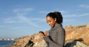 woman in gray long sleeve shirt holding smartphone and sitting on the rock formation