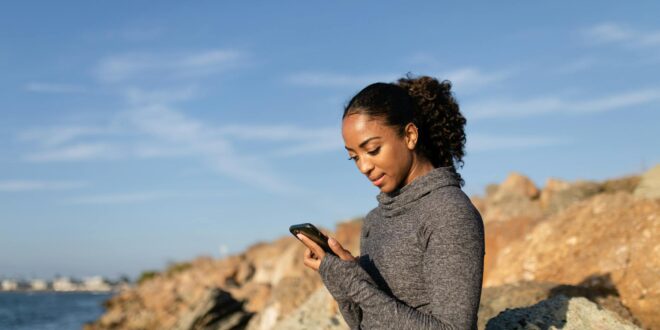 woman in gray long sleeve shirt holding smartphone and sitting on the rock formation