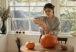 woman in gray sweater carving orange pumpkin