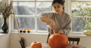 woman in gray sweater carving orange pumpkin