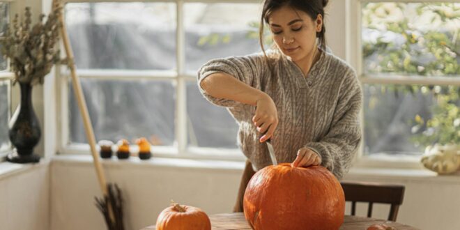 woman in gray sweater carving orange pumpkin