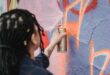 close up shot of a woman doing graffiti on a wall using a spray paint