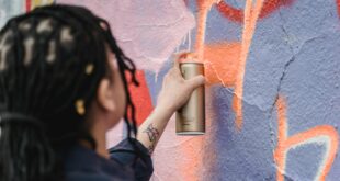 close up shot of a woman doing graffiti on a wall using a spray paint
