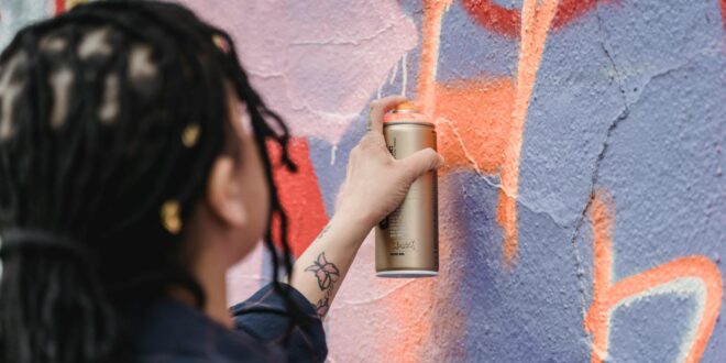 close up shot of a woman doing graffiti on a wall using a spray paint